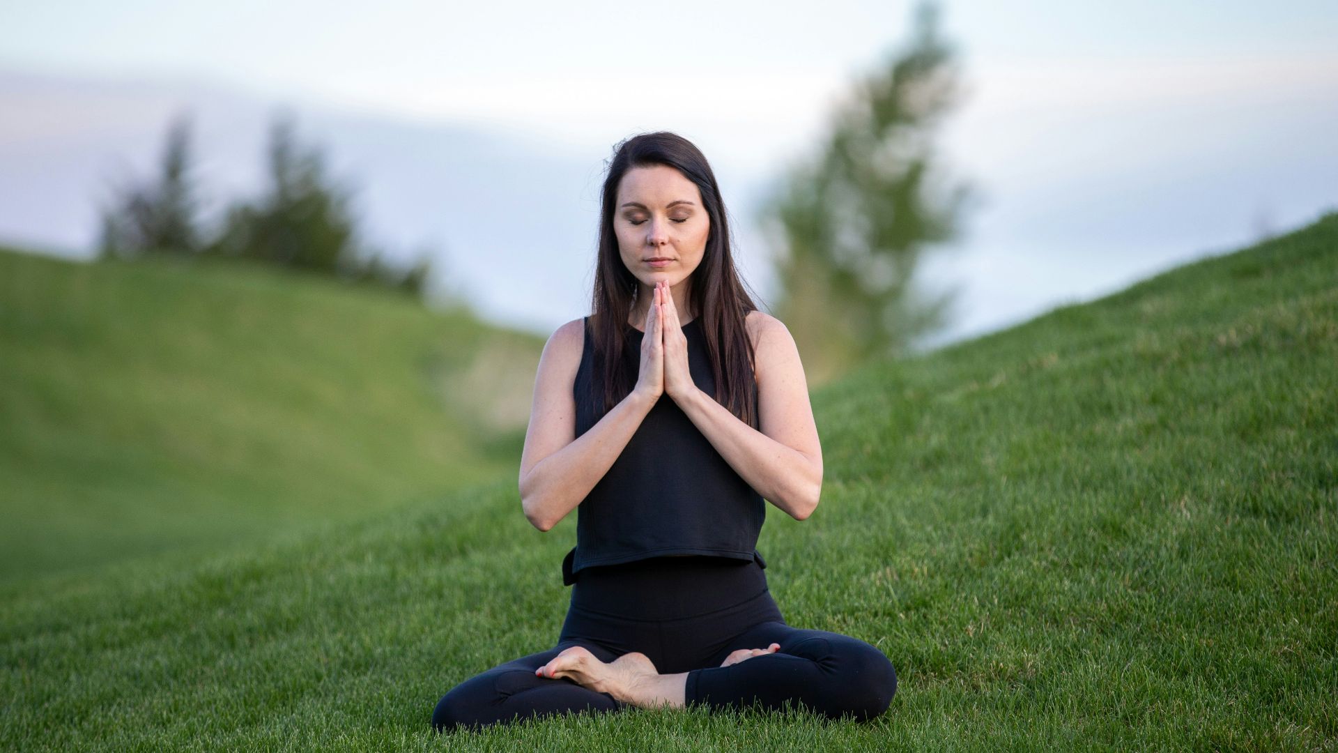 woman in black tank top and black pants sitting on green grass field during daytime