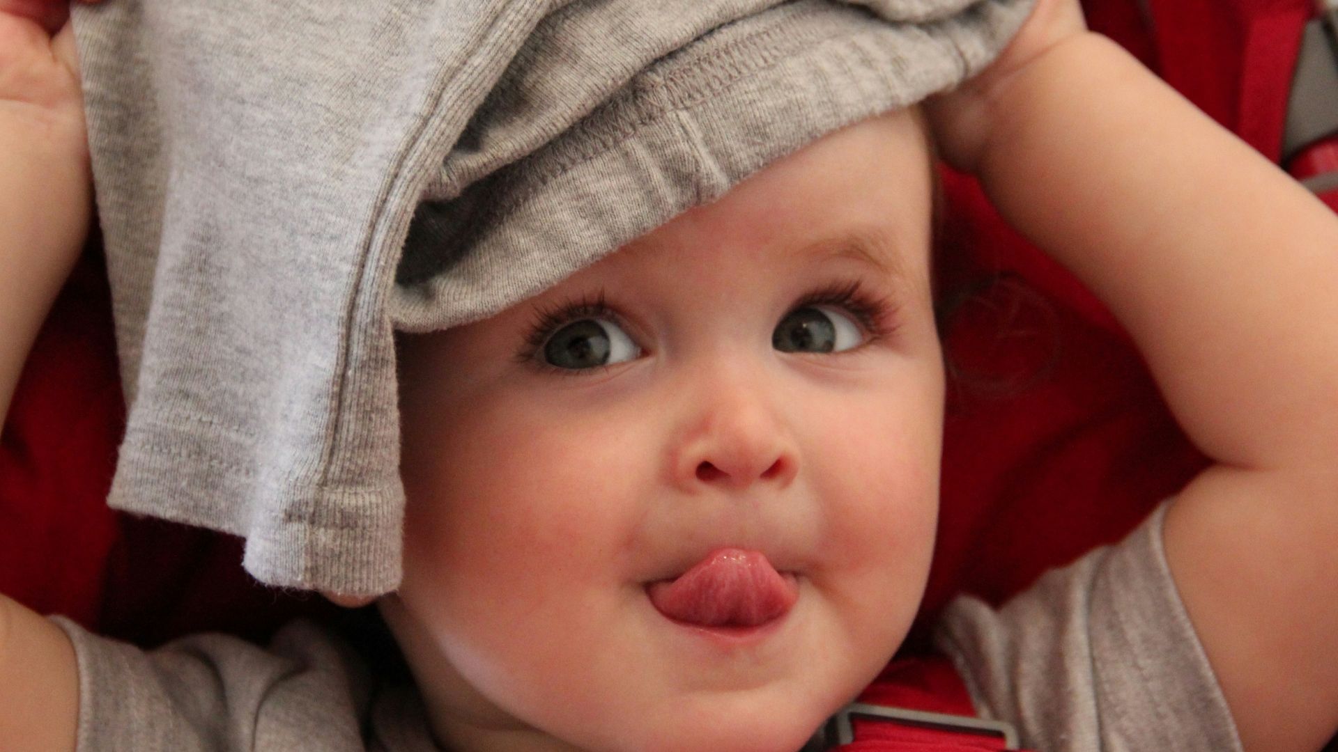 baby in red shirt lying on red textile