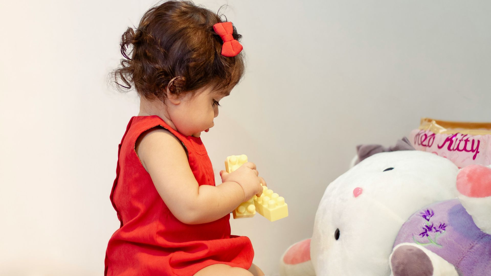 a little girl in a red dress playing with a stuffed animal