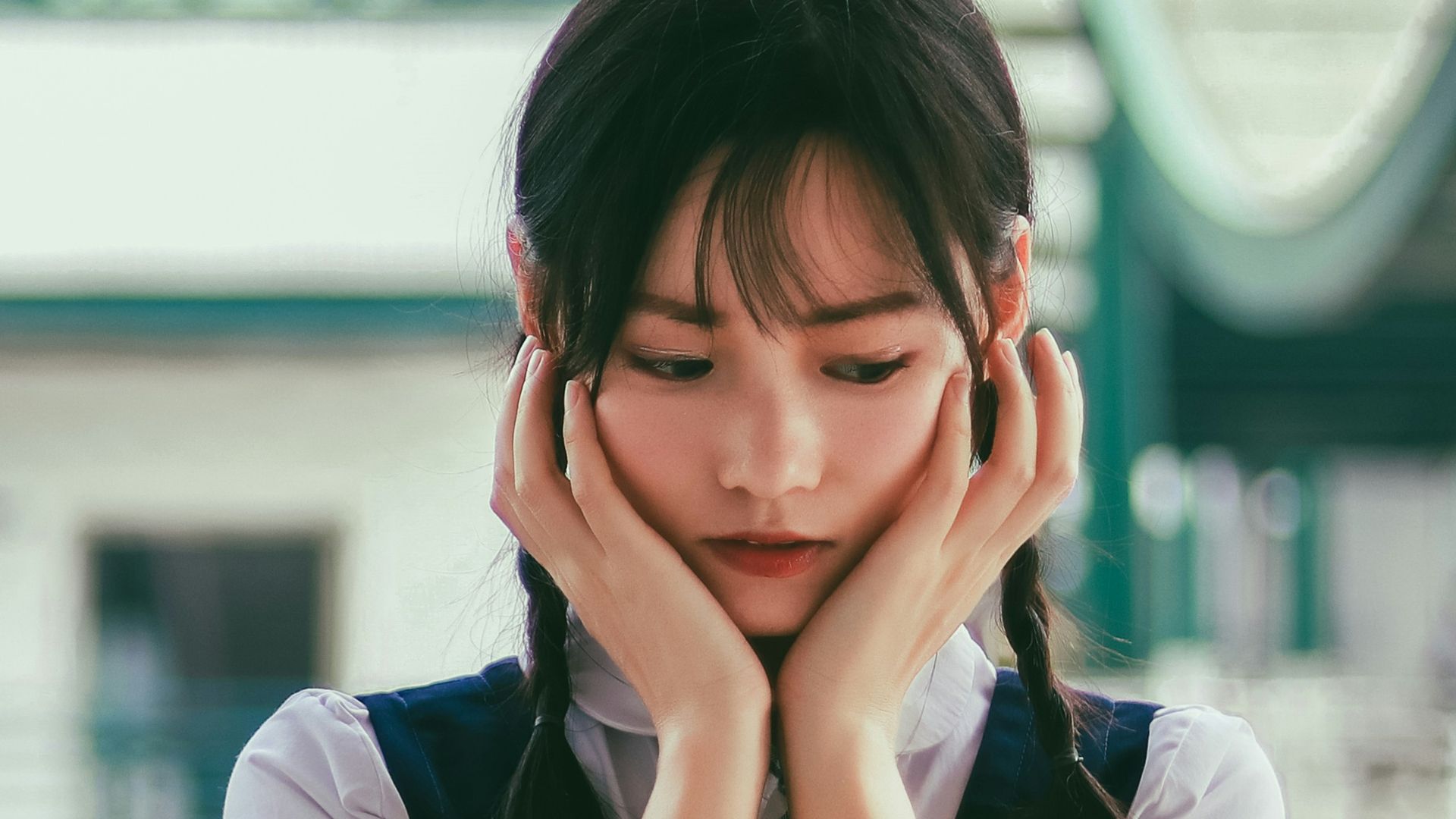 woman holding her face standing near white and green concrete building