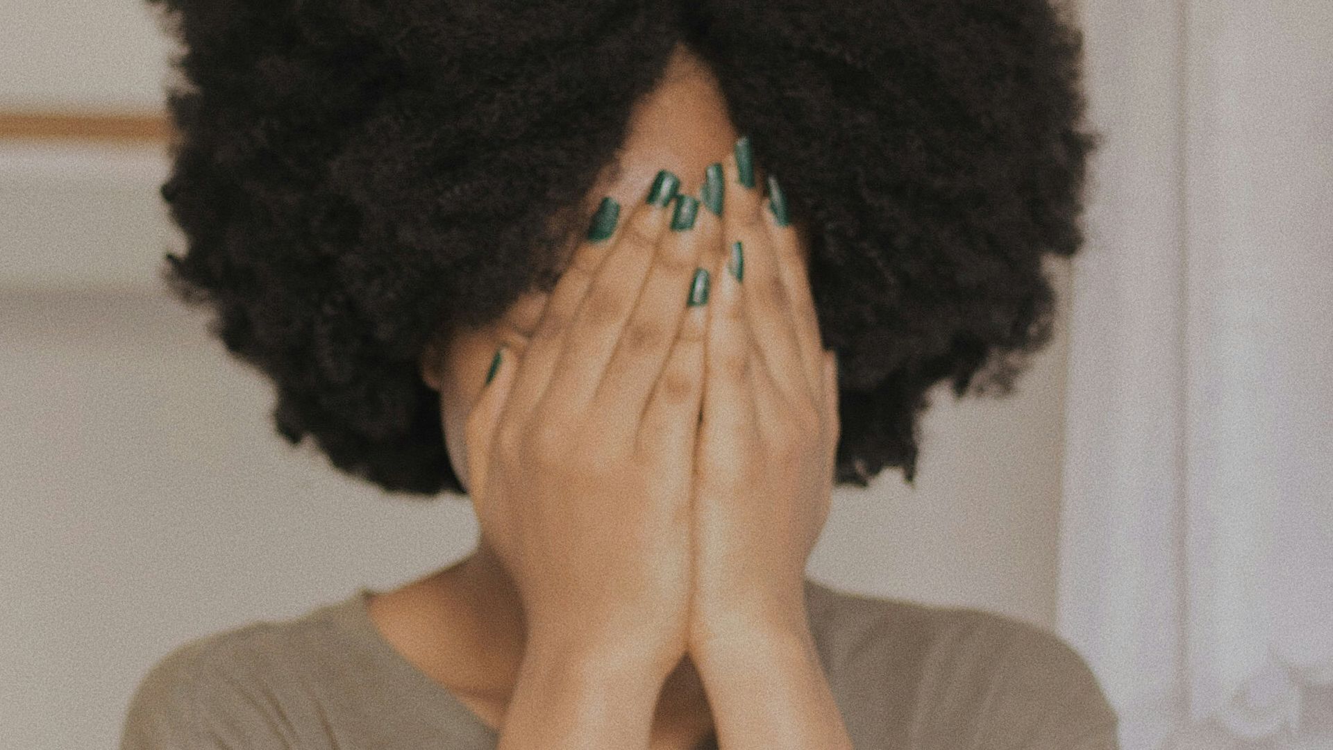 woman in gray t-shirt covering face with both hands