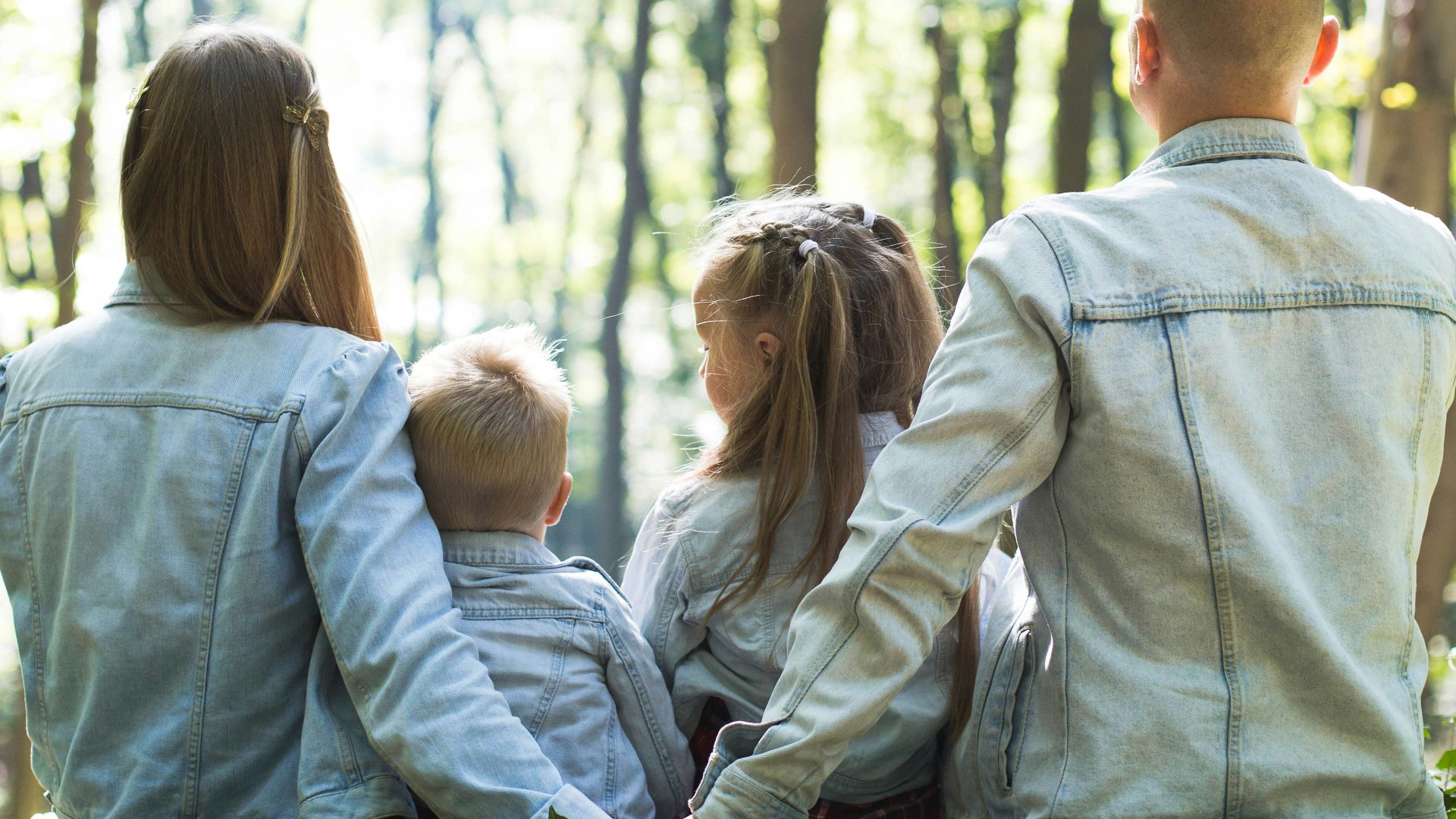 man and woman holding hands together with boy and girl looking at green trees during day