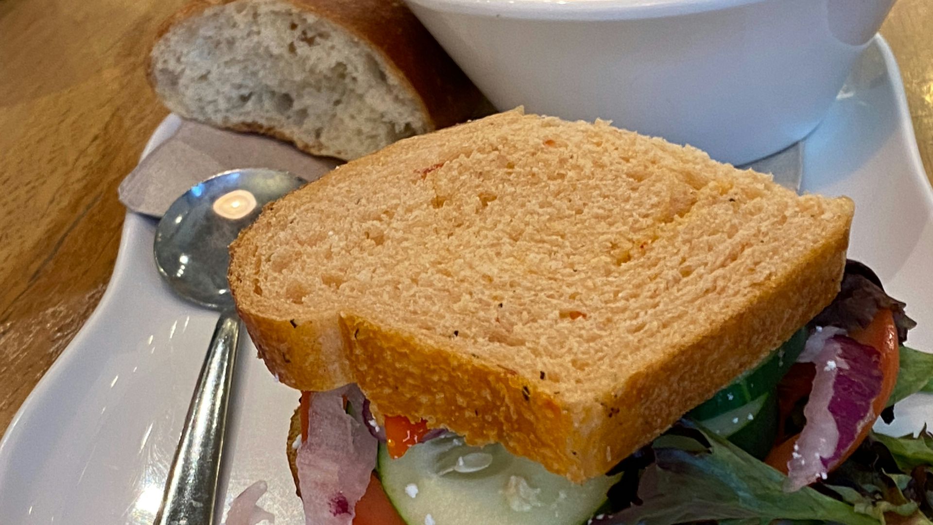 A white plate topped with a sandwich and a bowl of soup