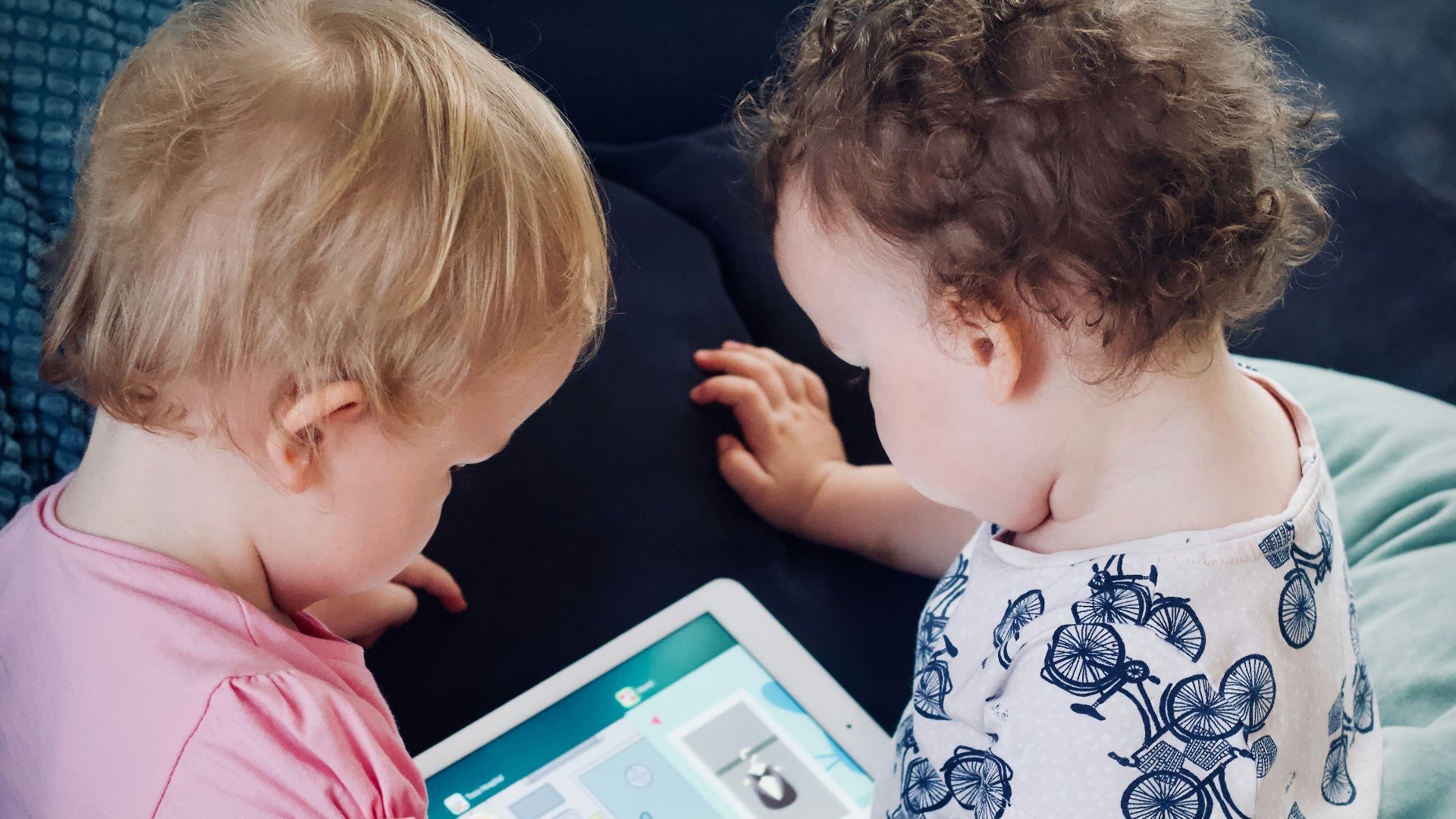 two toddlers sitting on sofa while using tablet computer