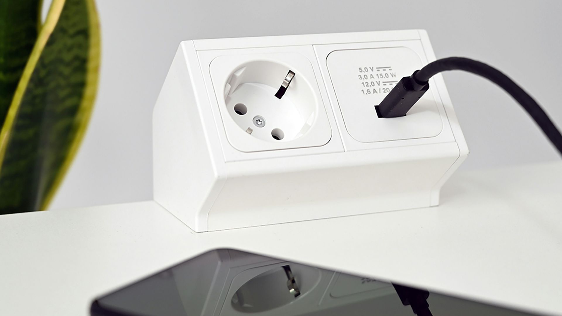 a phone charging on a white table next to a plant