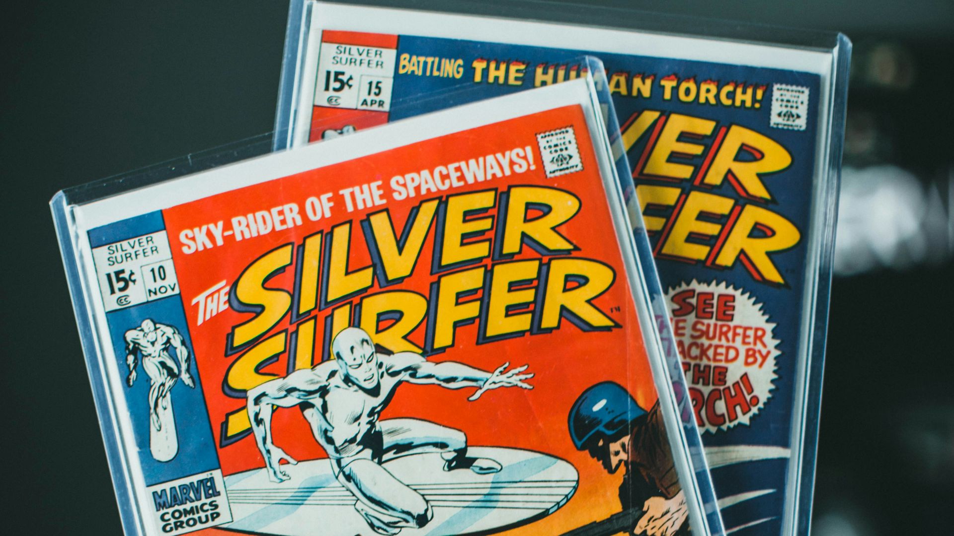 a person holding up two silver surfer comics