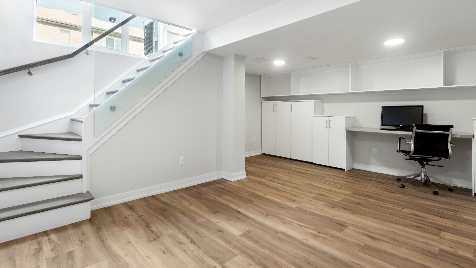 an empty room with a desk, computer, and stairs