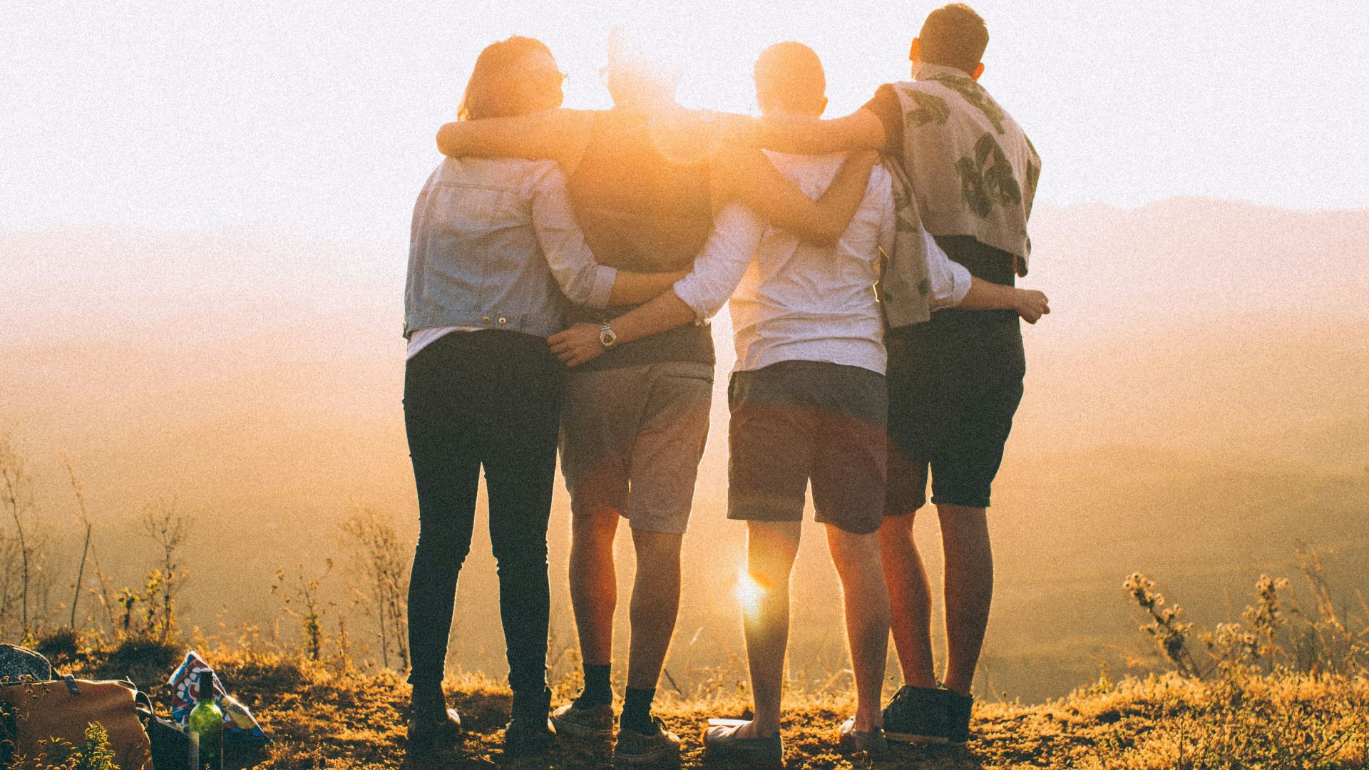 four person hands wrap around shoulders while looking at sunset
