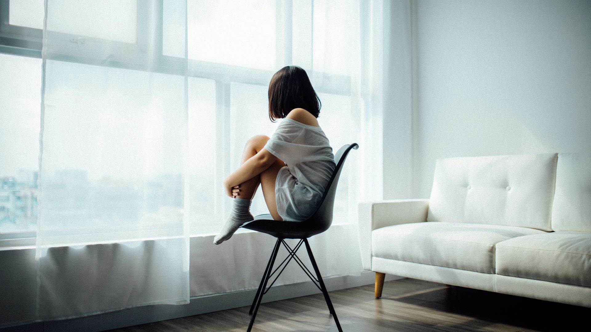 woman sitting on black chair in front of glass-panel window with white curtains