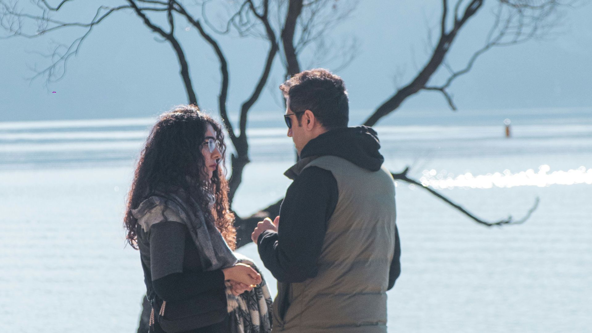 A man and woman standing on a beach next to a tree