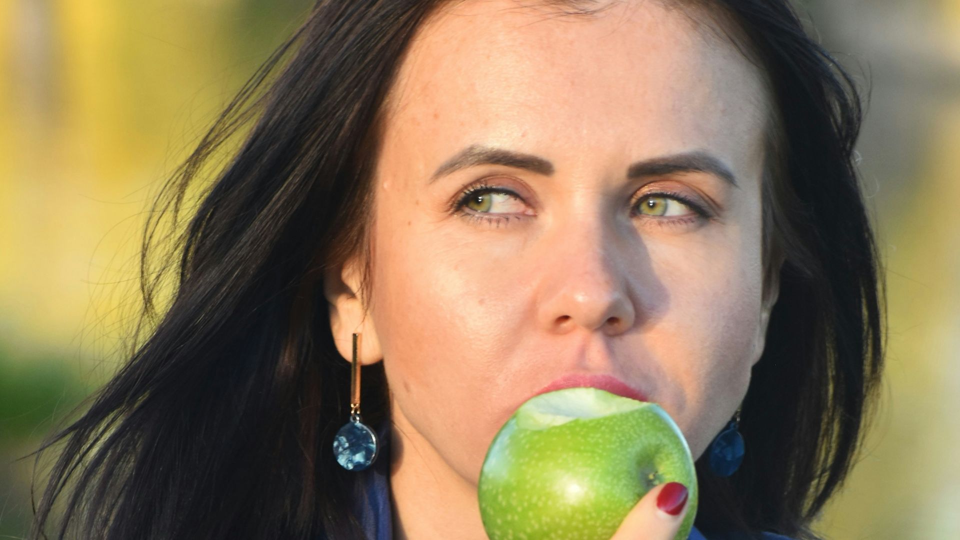 a woman in a blue shirt eating an apple