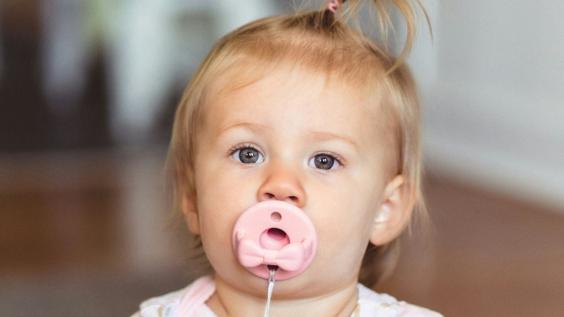a little girl sitting on the floor with a pacifier in her mouth