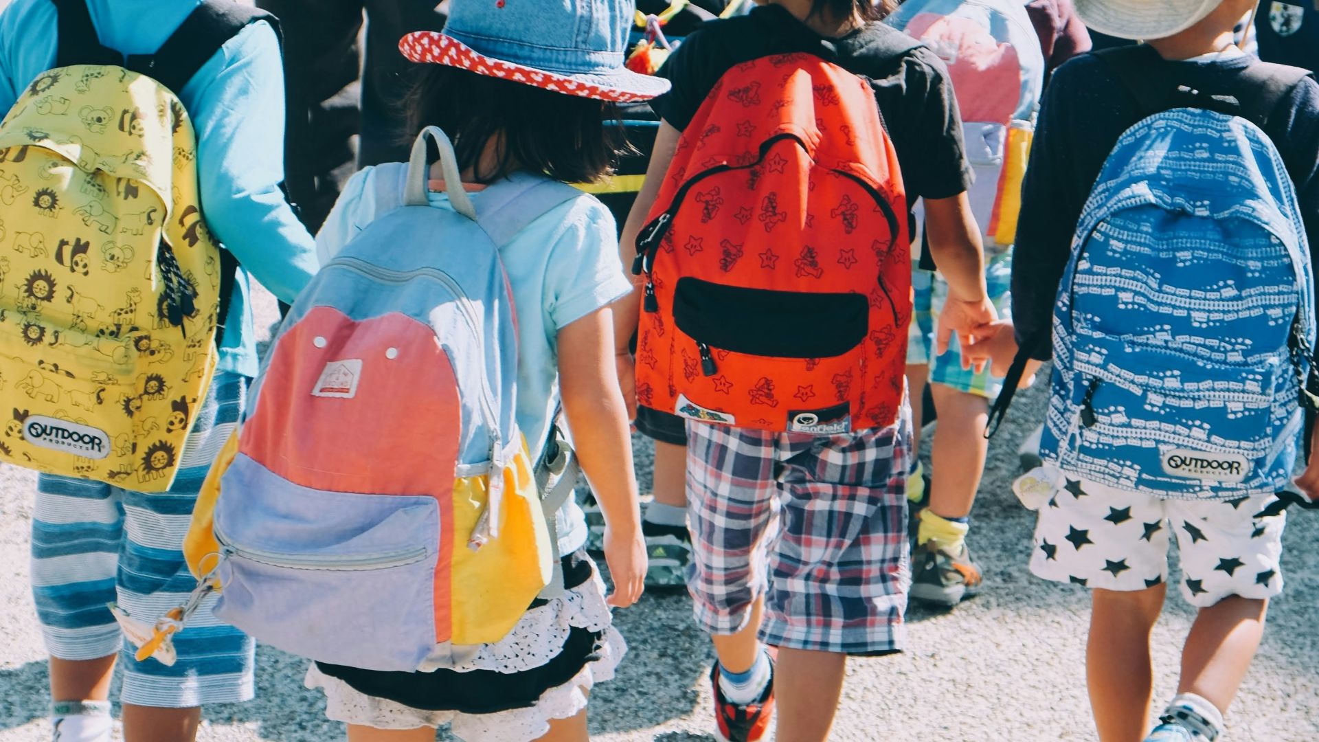 group of people wearing white and orange backpacks walking on gray concrete pavement during daytime