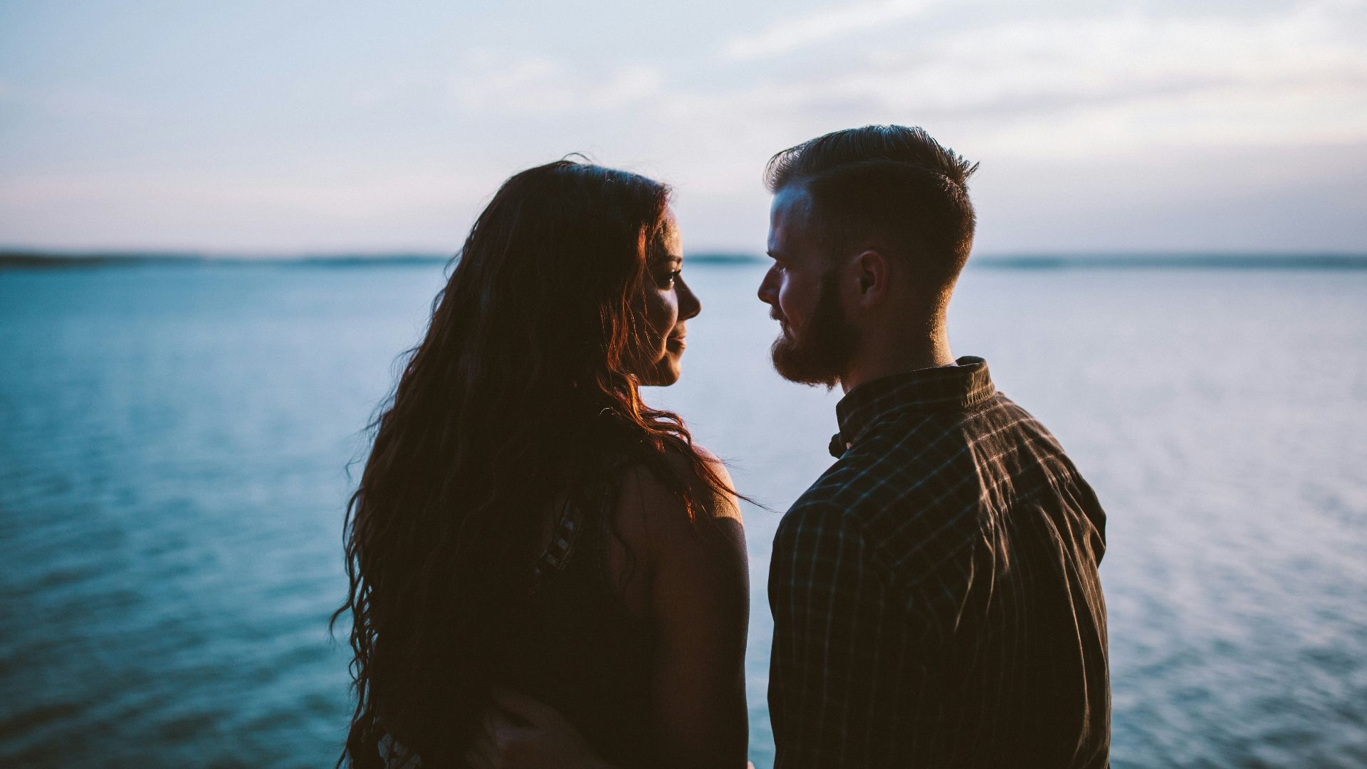 man and woman standing while looking each other near body of water