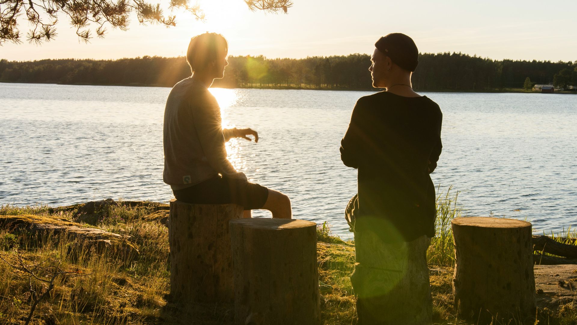 man in black jacket standing beside body of water during sunset