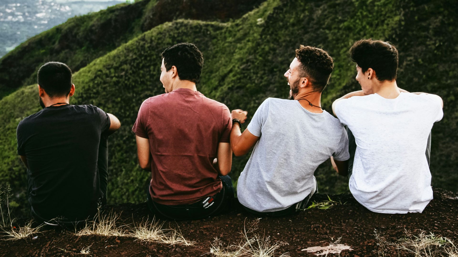 row of four men sitting on mountain trail