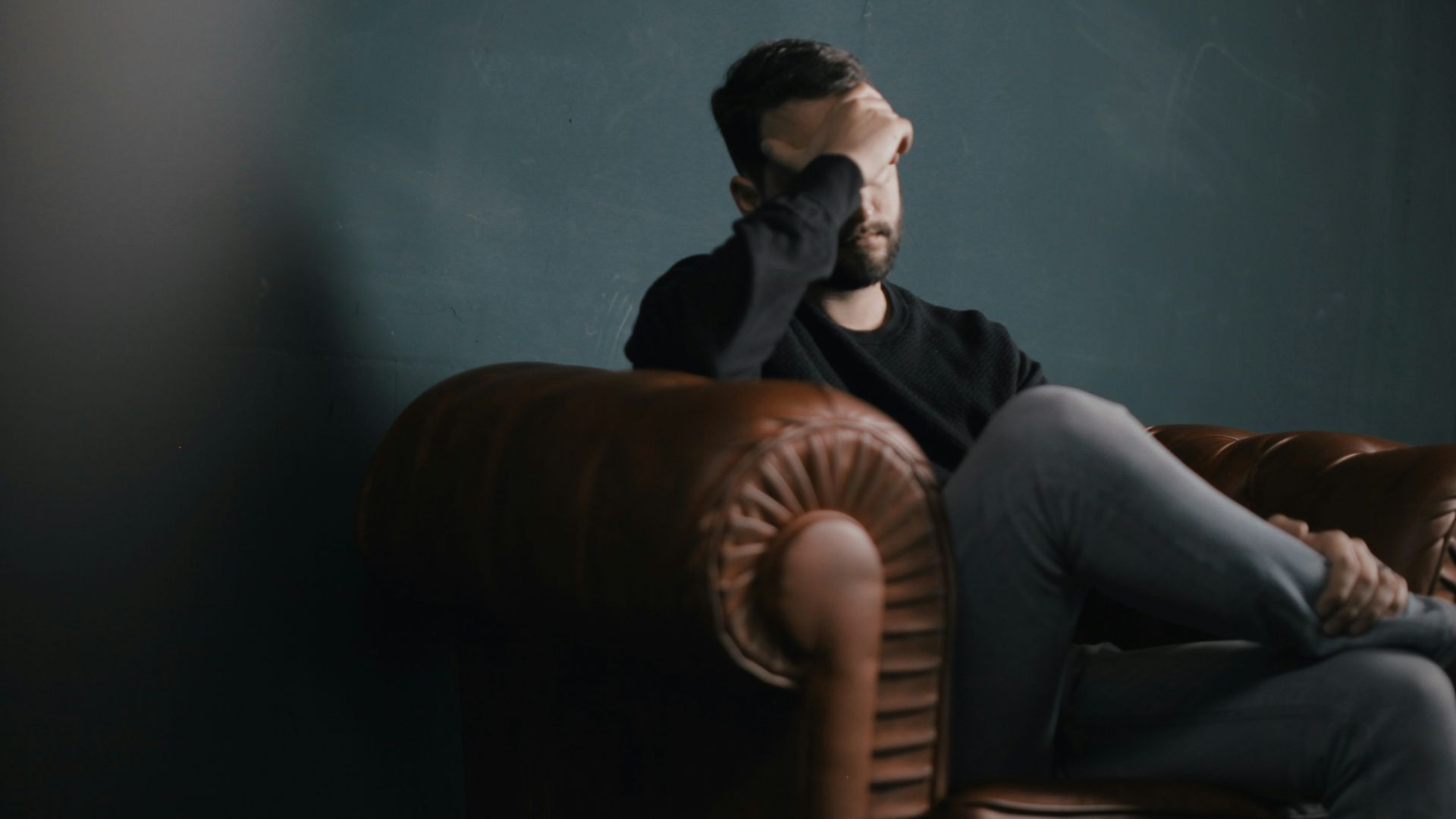 a man holds his head while sitting on a sofa