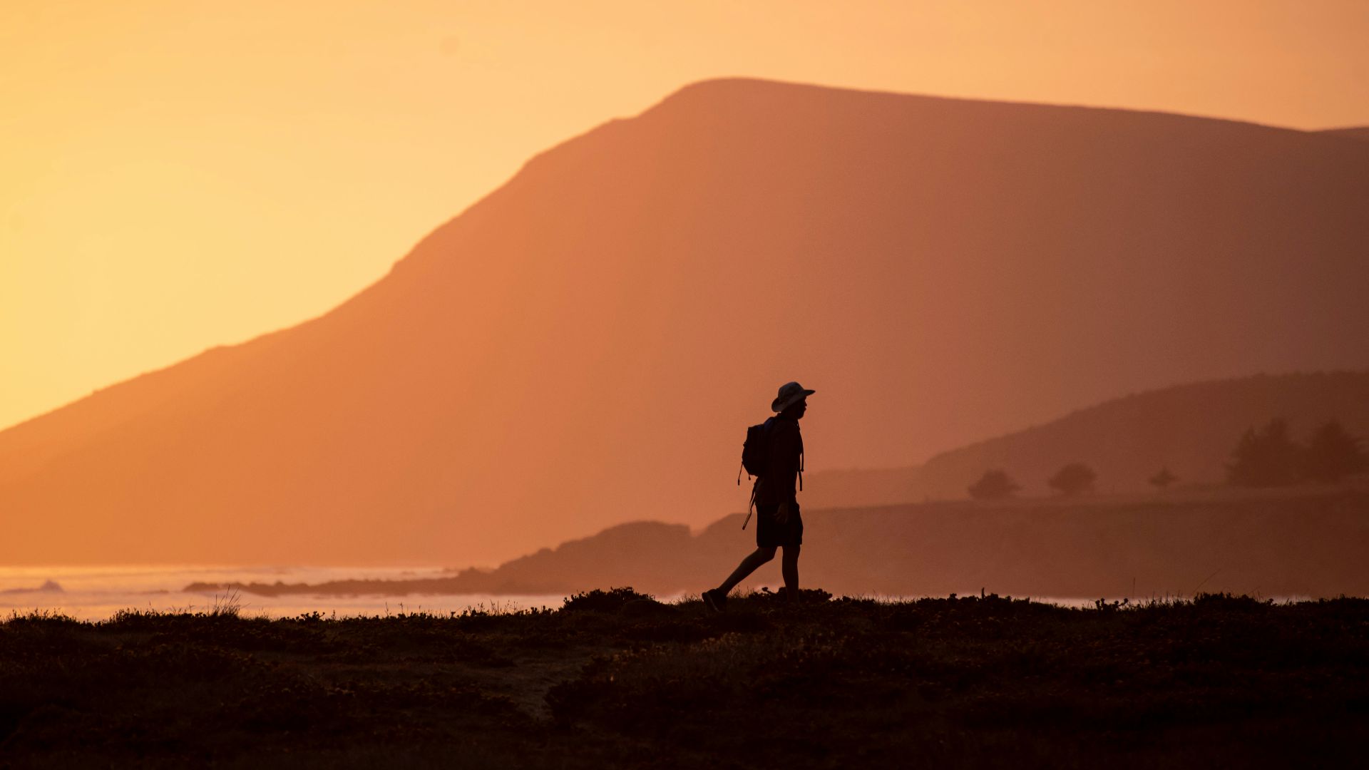 silhouette of man standing on hill during sunset