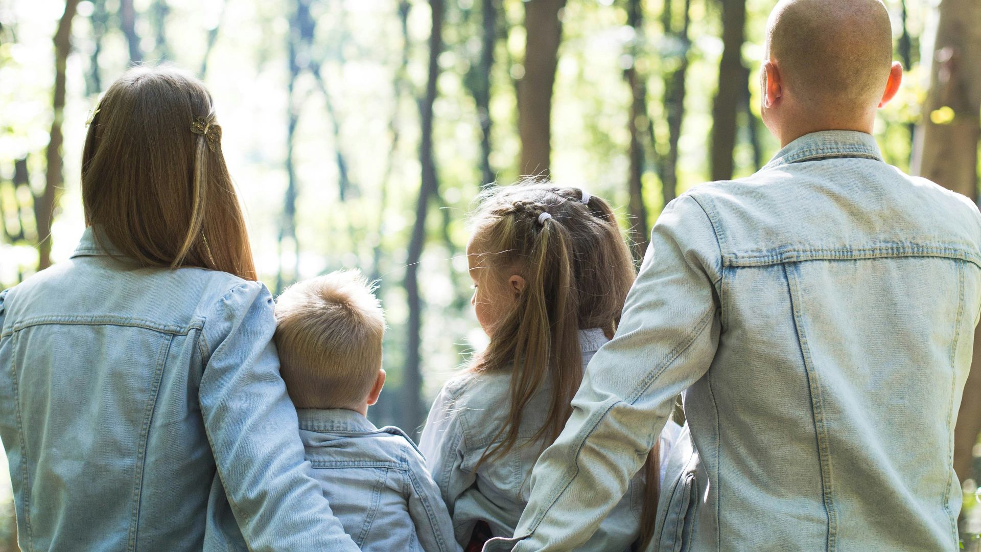 man and woman holding hands together with boy and girl looking at green trees during day