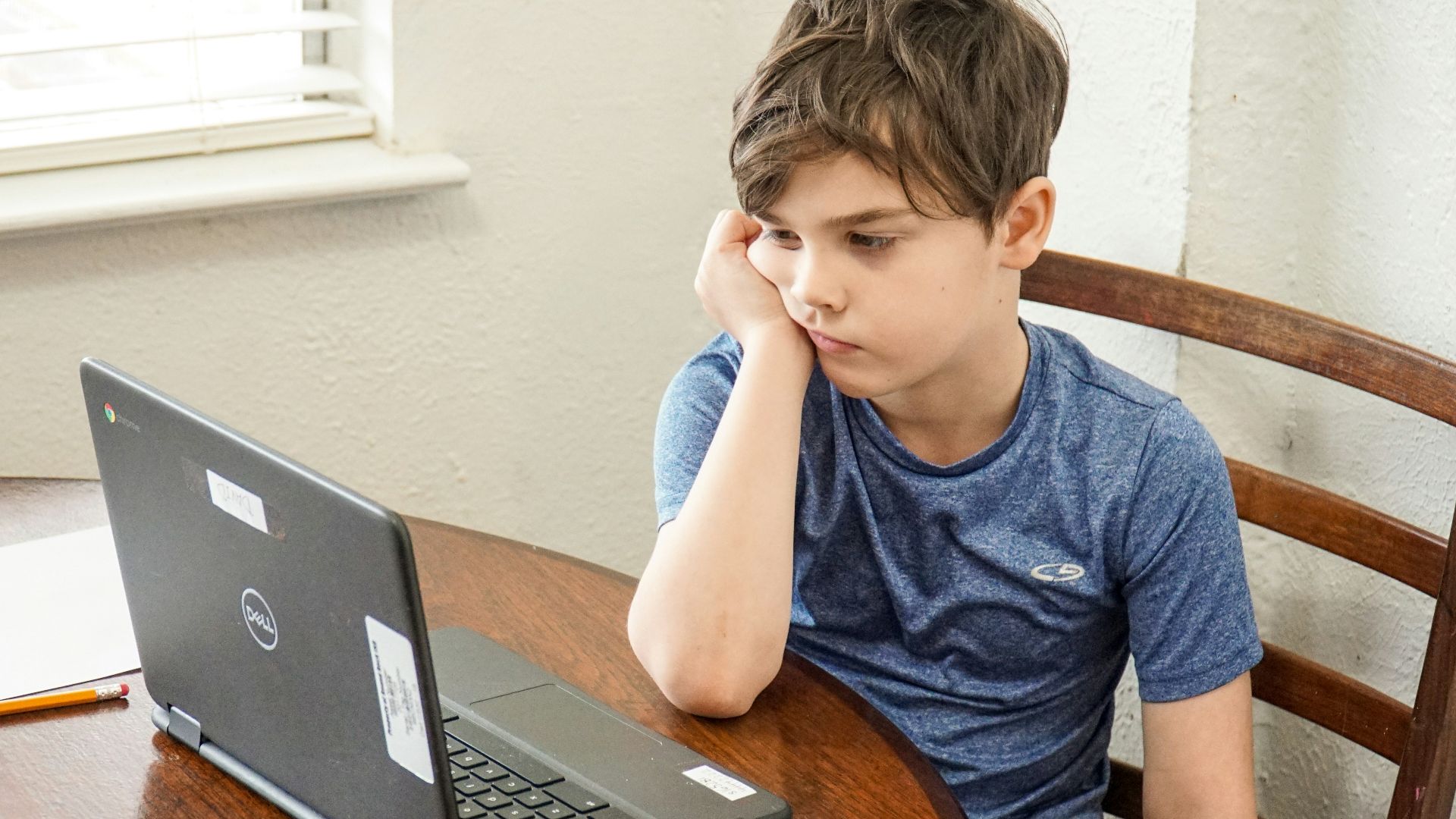 boy in blue crew neck t-shirt using macbook pro on brown wooden table
