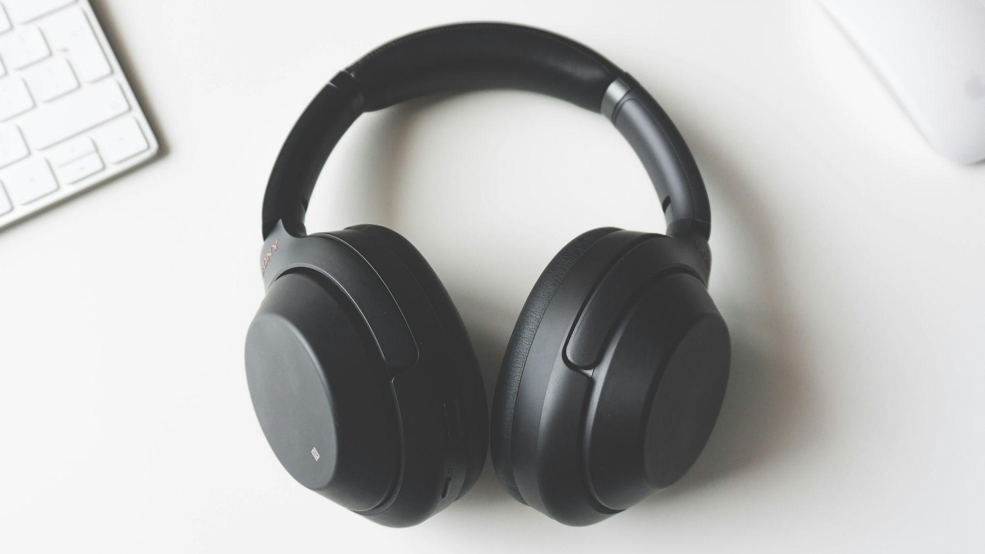 black wireless headphones between Apple Keyboard and Apple Magic Mouse on white surface