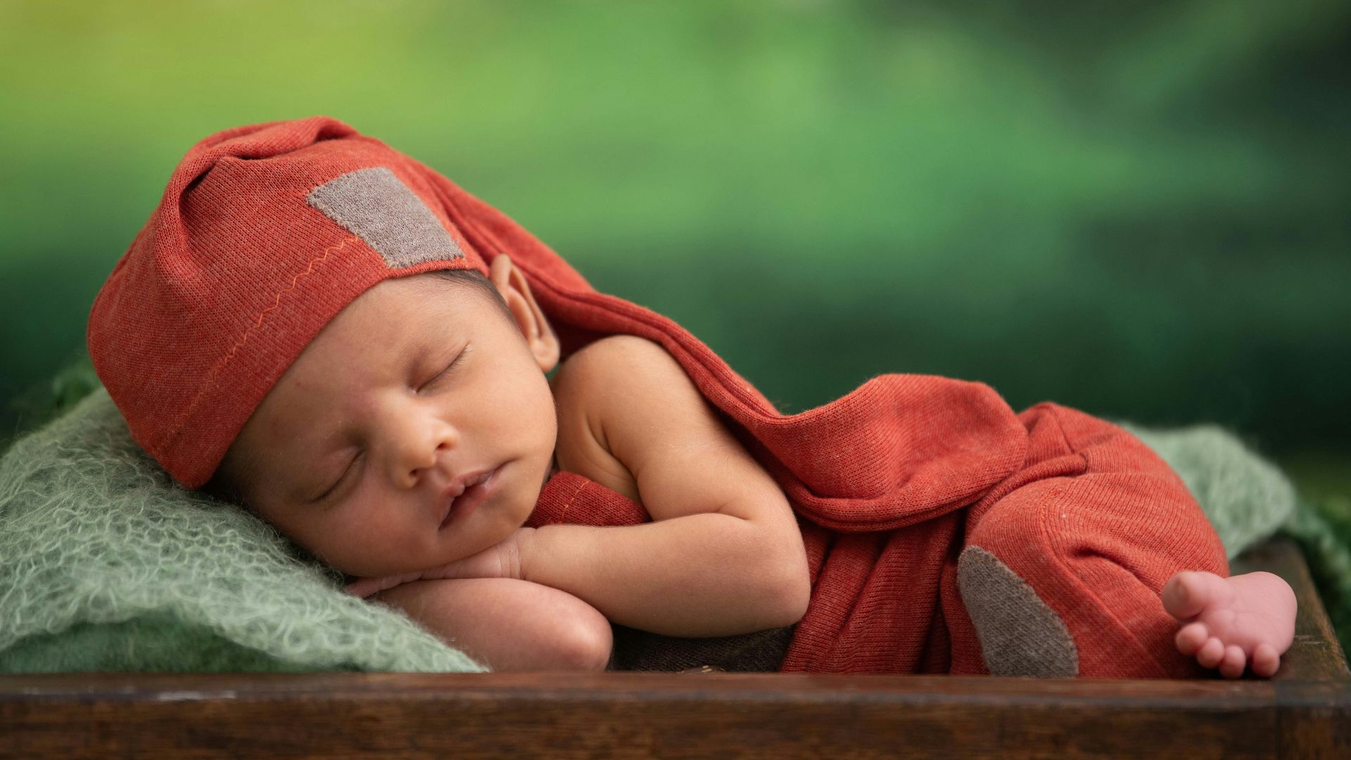 baby in red blanket lying on green textile