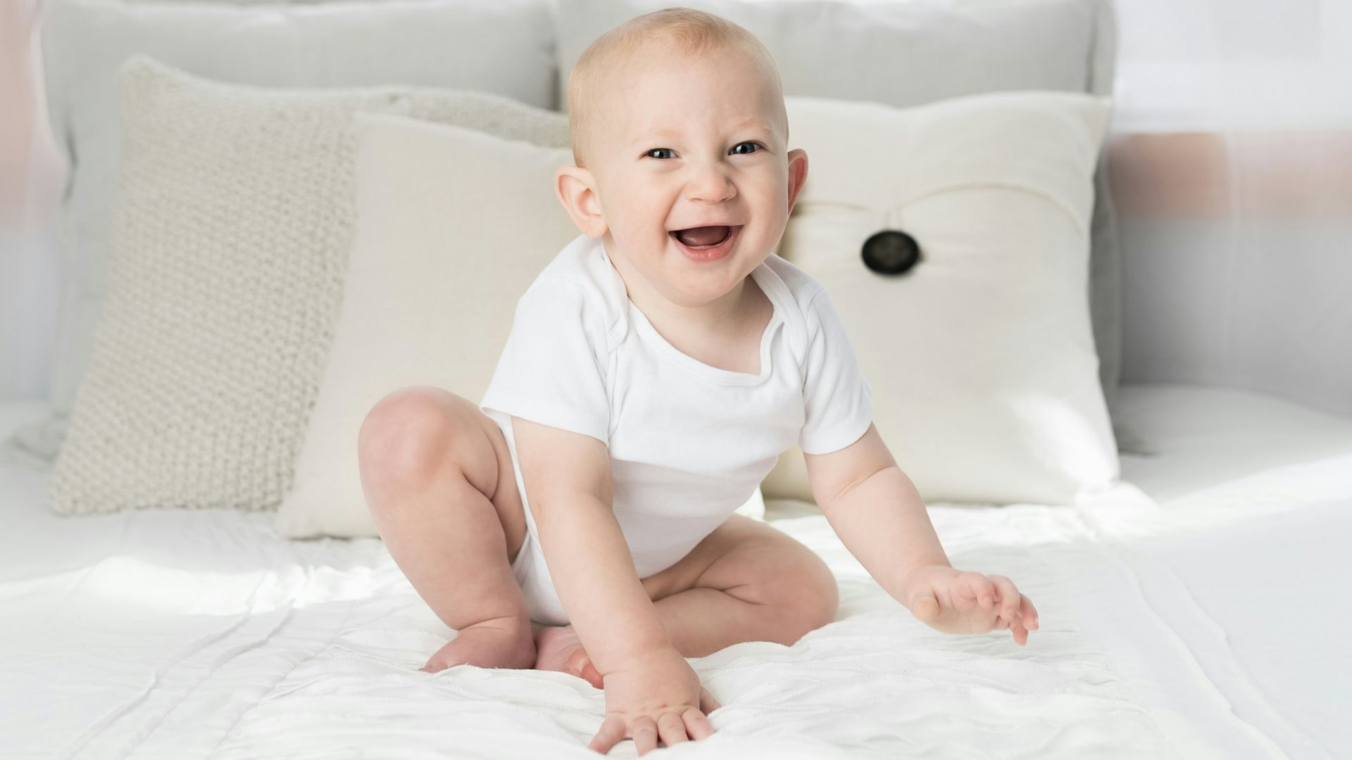 smiling baby sitting on white bed