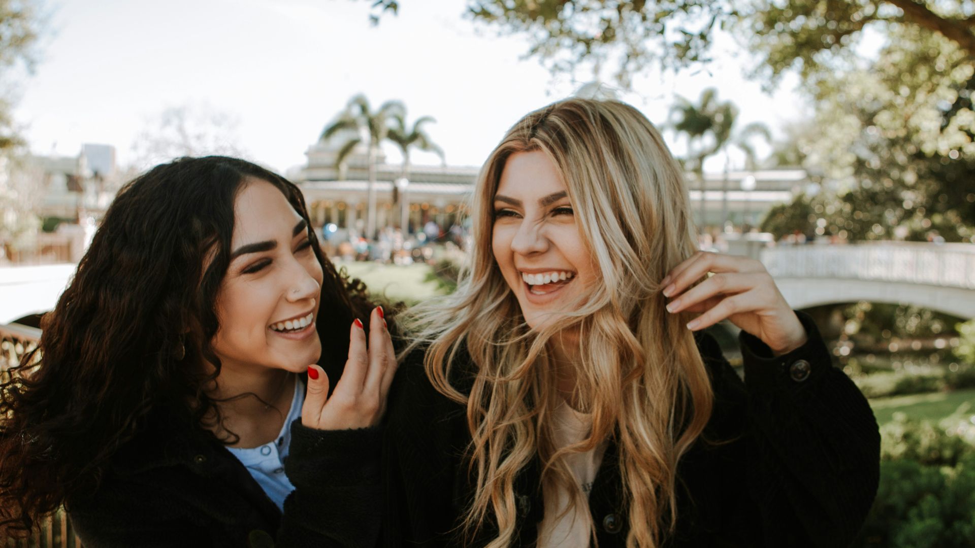 2 women smiling and standing near trees during daytime