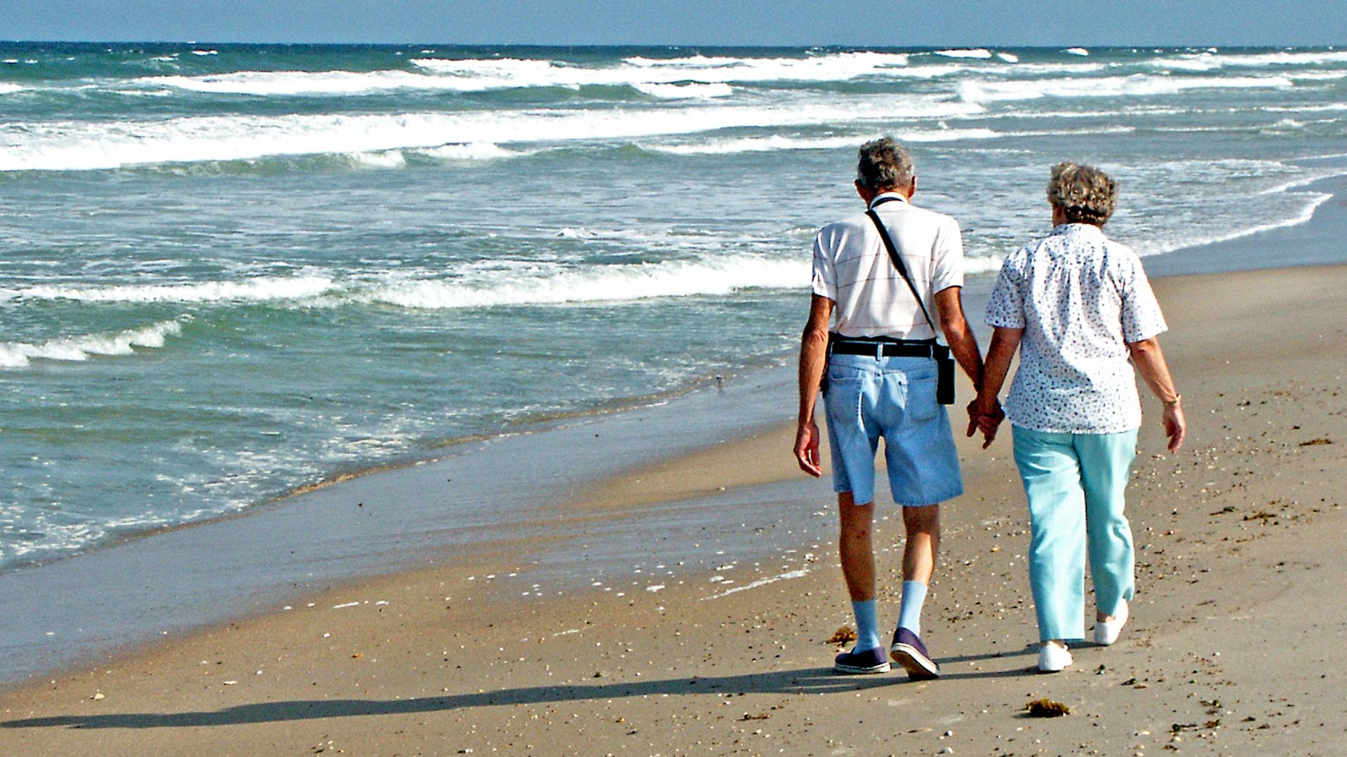 Couple walks hand-in-hand on the beach.