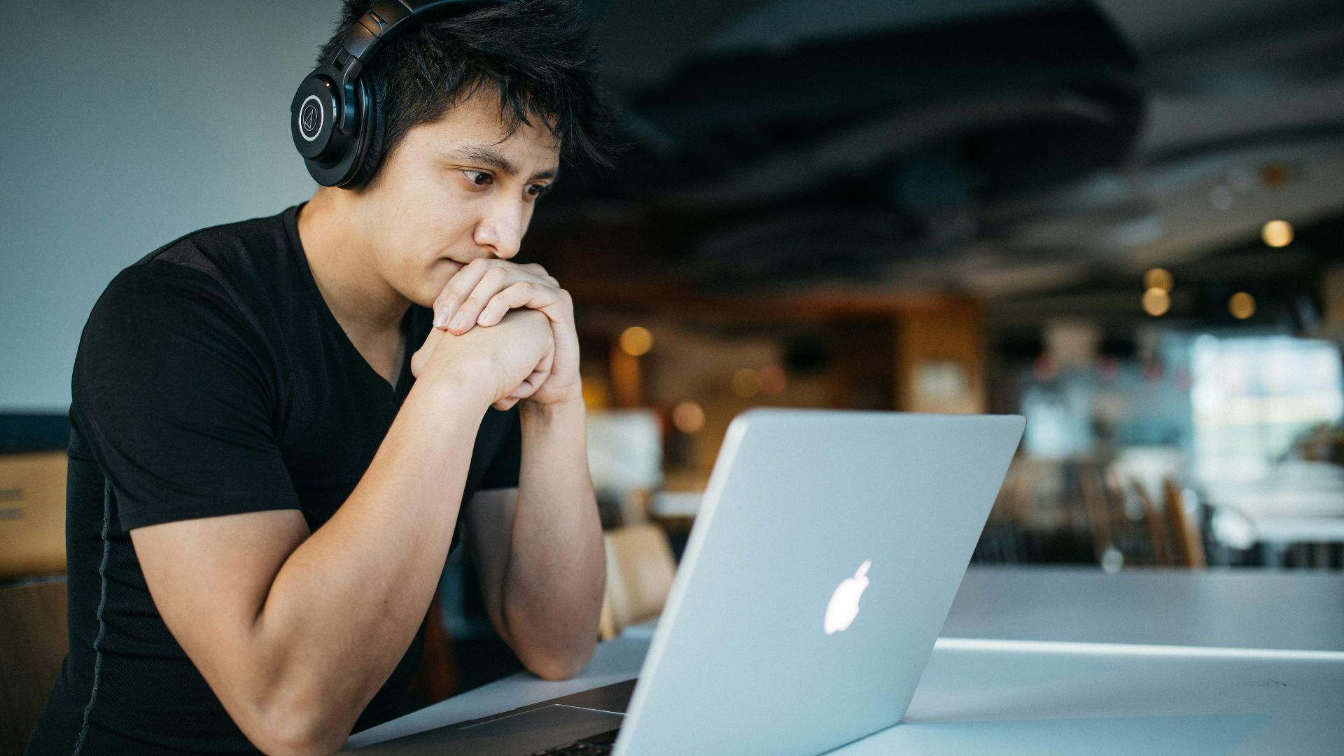 man wearing headphones while sitting on chair in front of MacBook