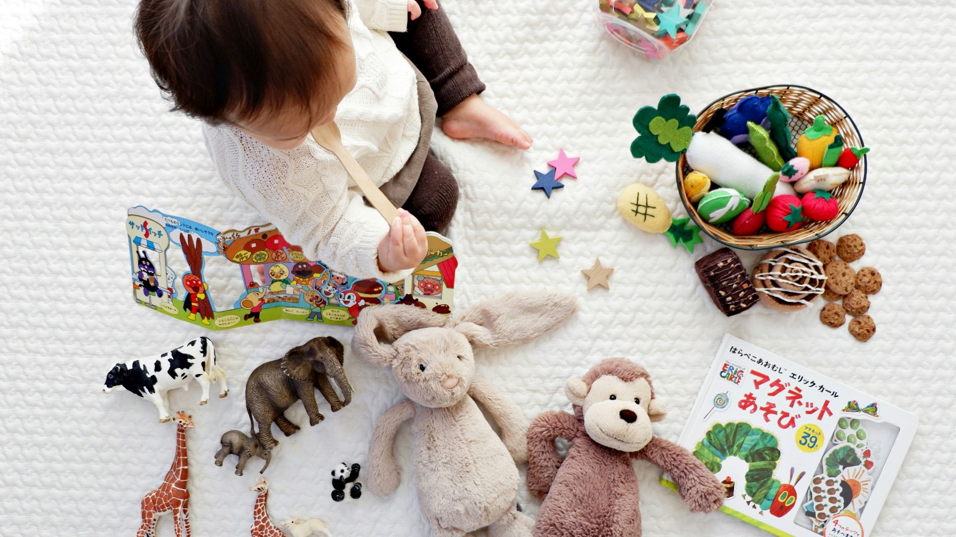 boy sitting on white cloth surrounded by toys