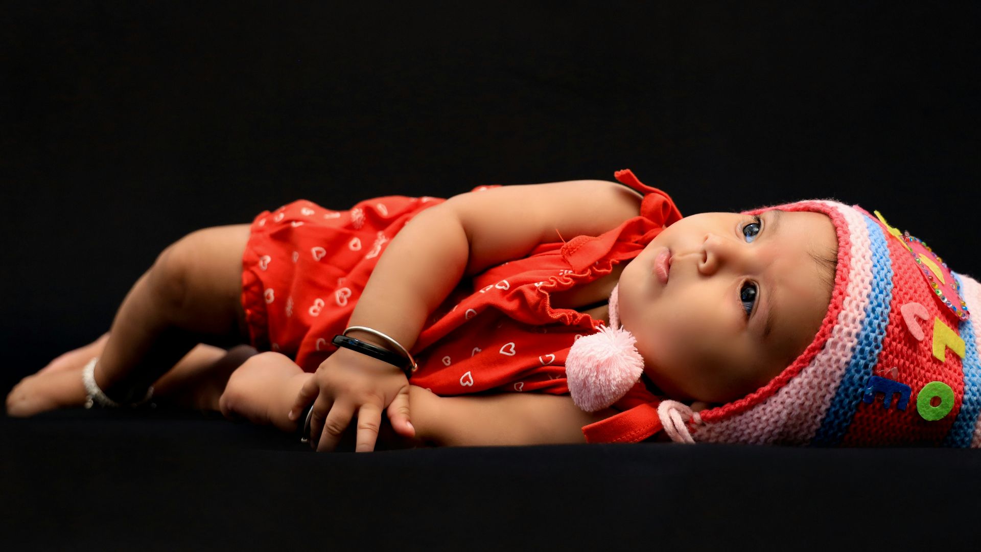 baby in red shirt lying on black textile