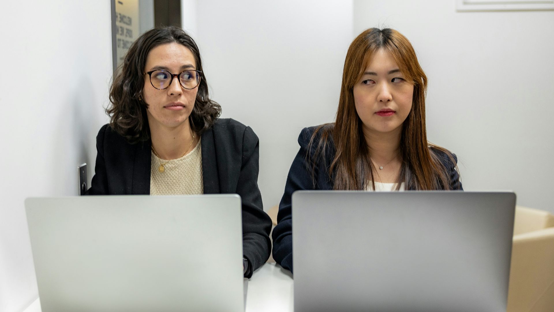 two women sitting at a table with laptops