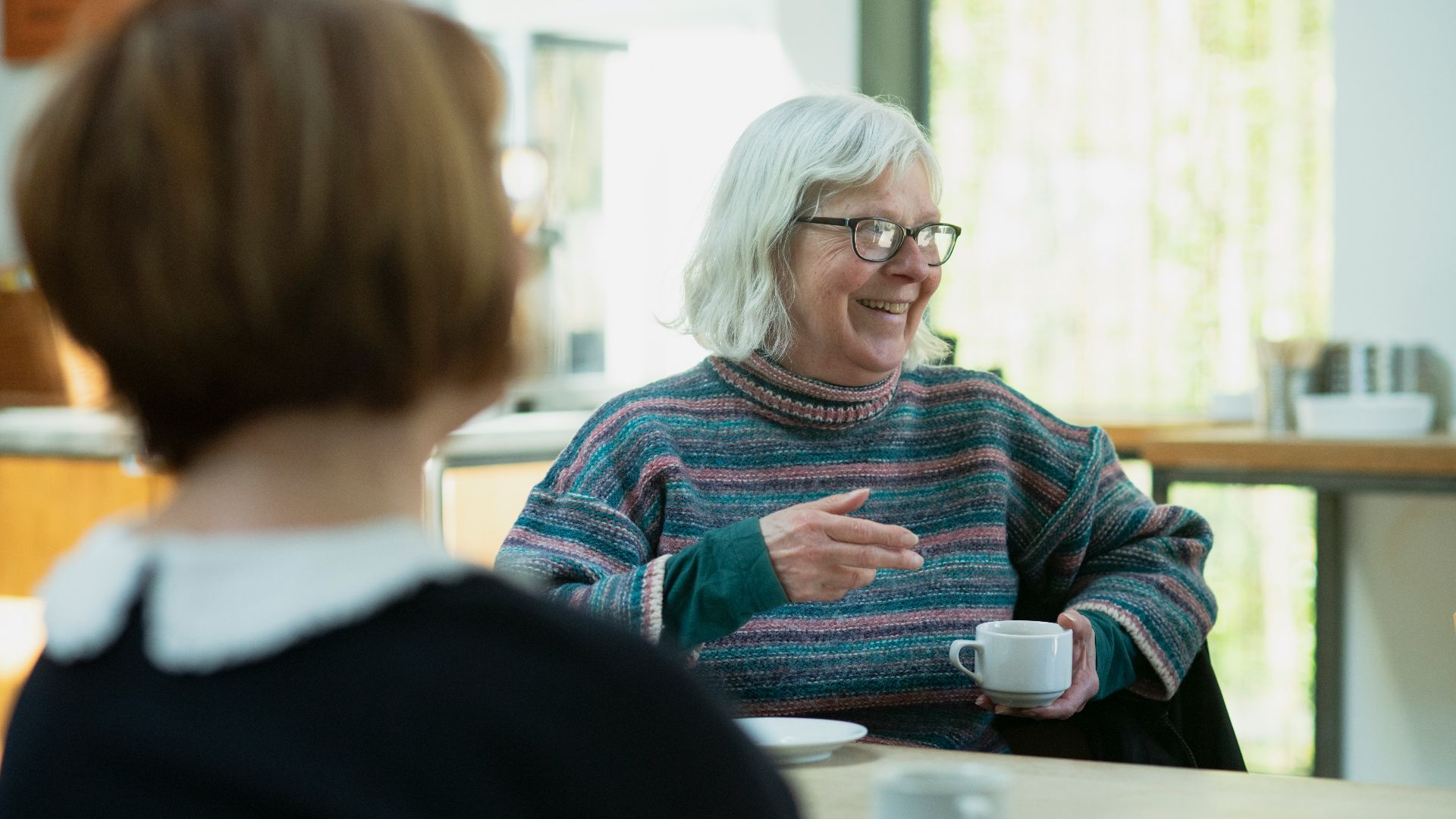 a woman sitting at a table talking to another woman