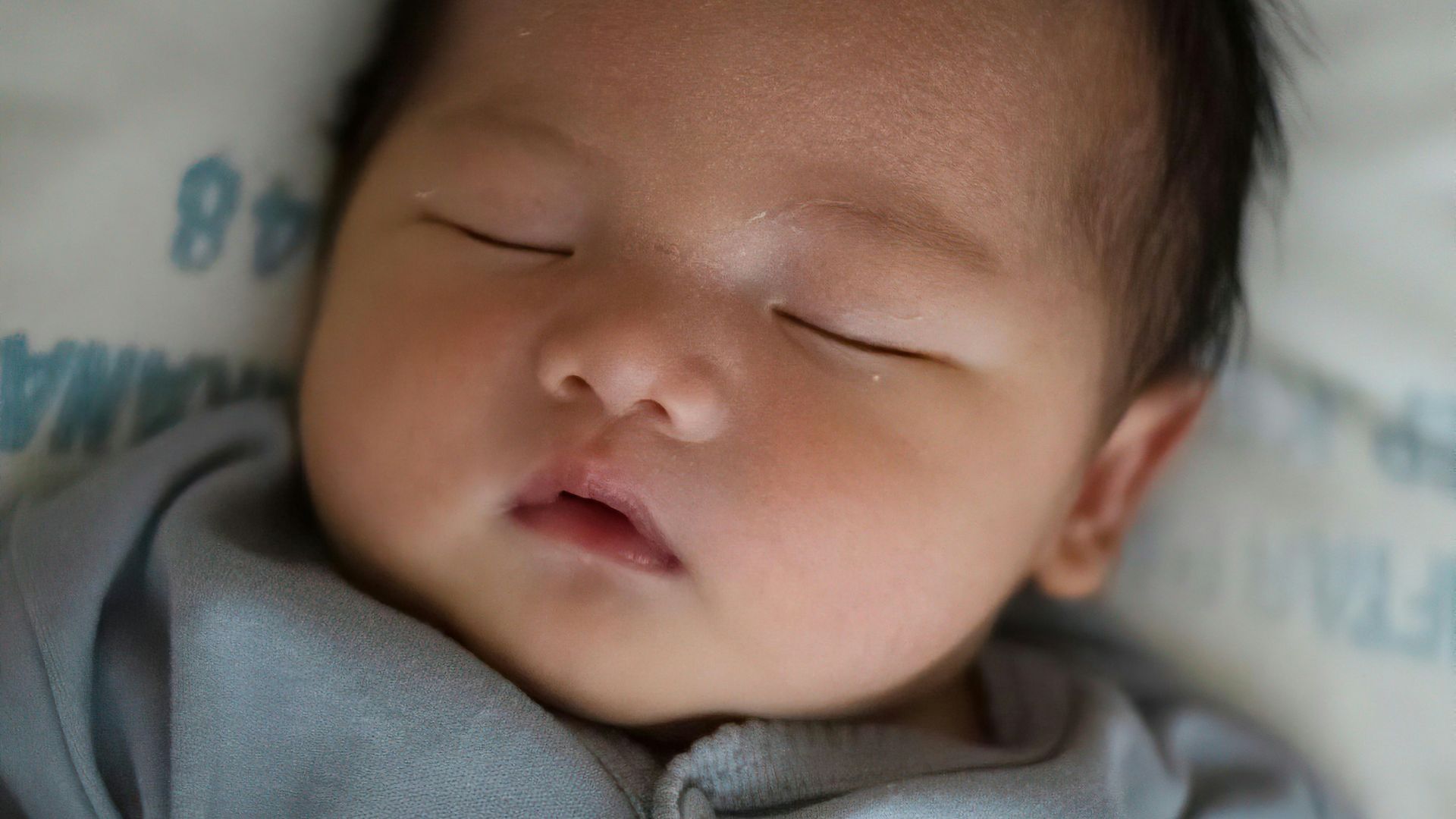 baby in gray onesie lying on bed