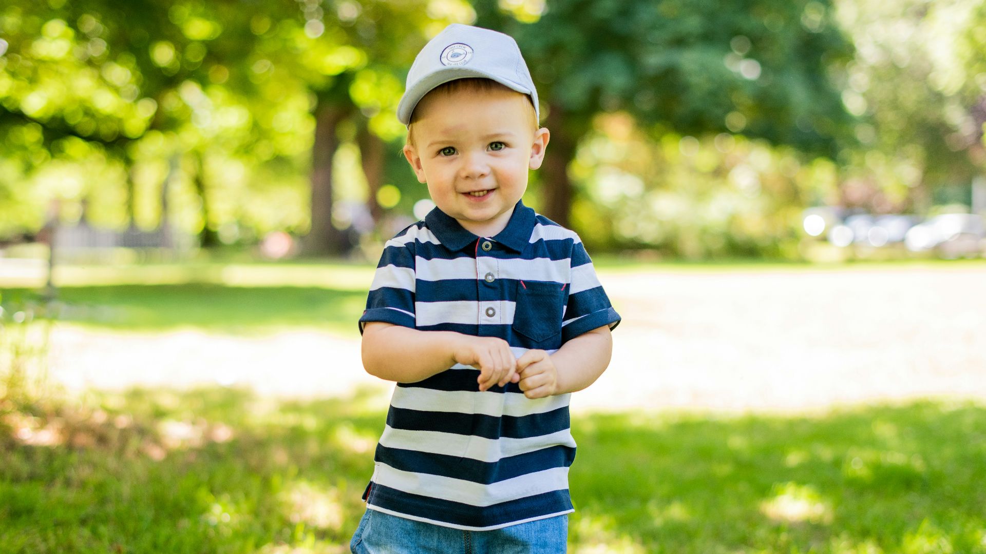 boy in black and white stripe polo shirt and blue denim shorts standing on green grass