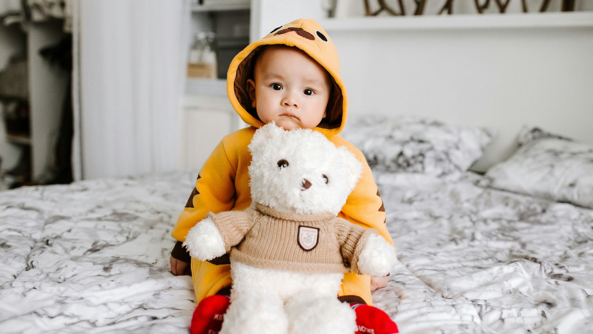toddler sitting on bed beside white bear plush toy