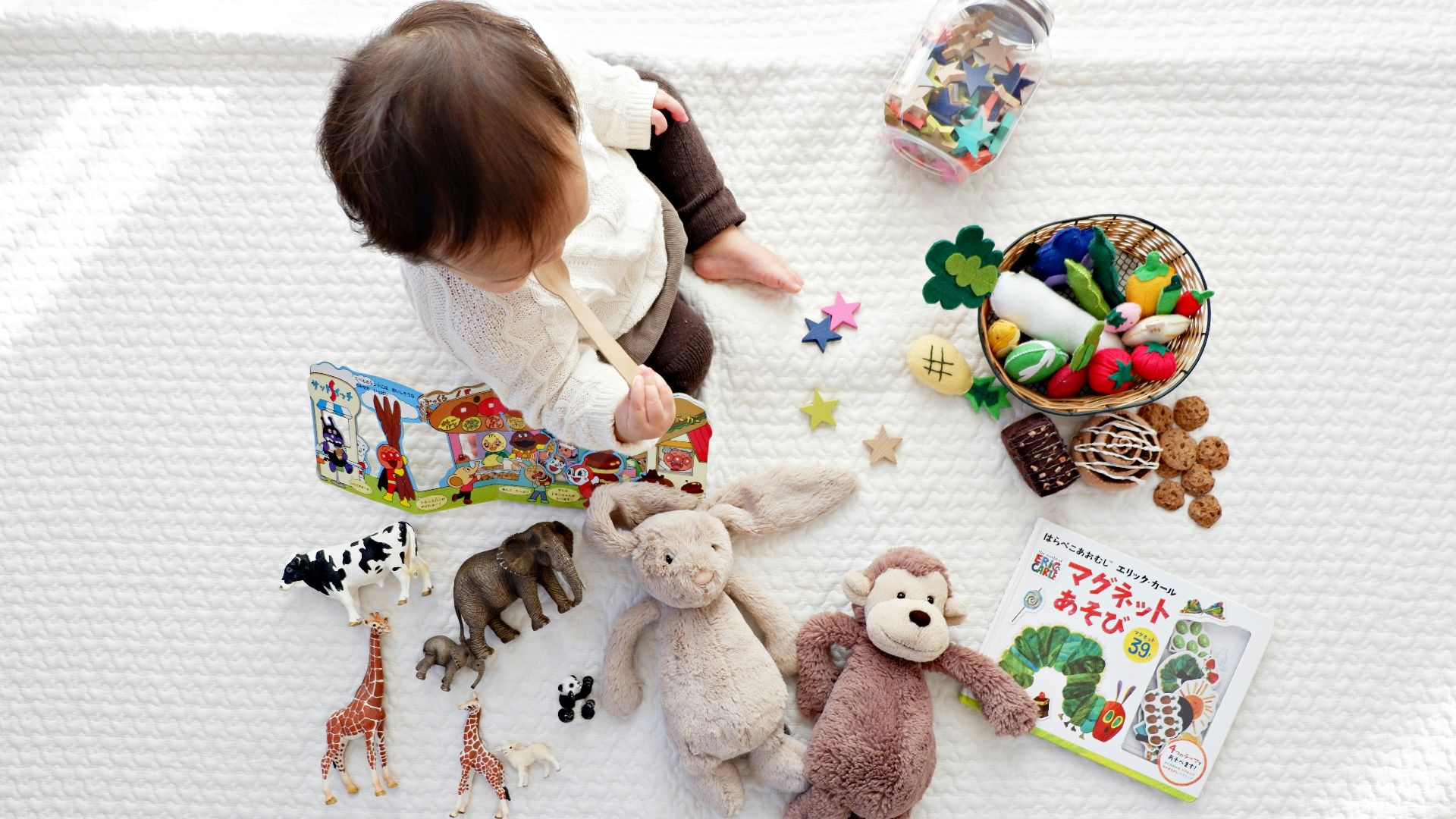 boy sitting on white cloth surrounded by toys