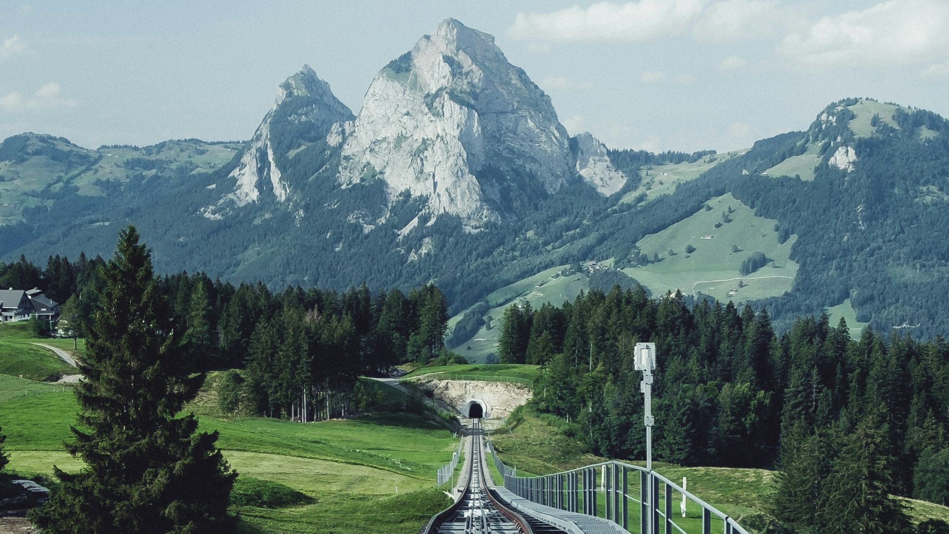 aerial photography of train railway near green field viewing mountain under white and blue skies during daytime
