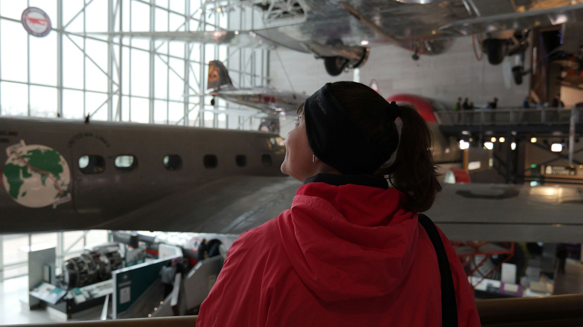 a woman in a red jacket looking at a plane