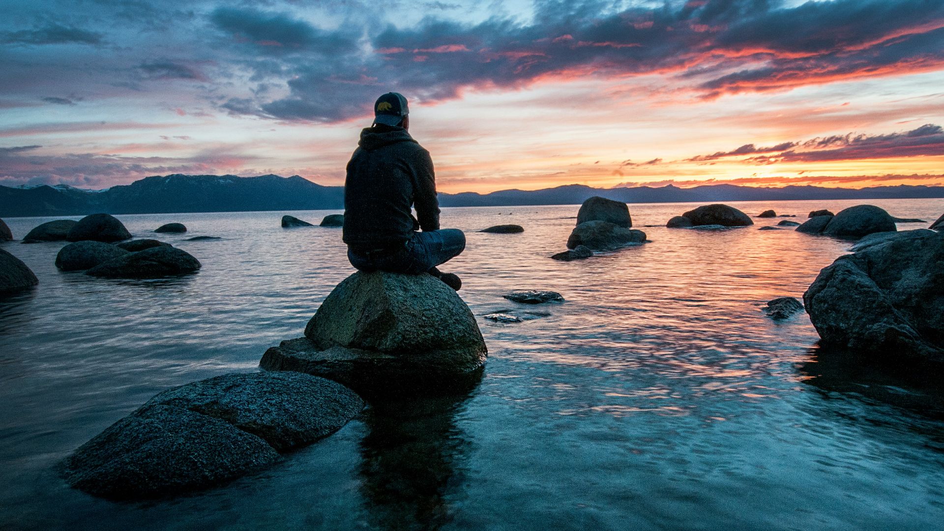 man sitting on rock surrounded by water
