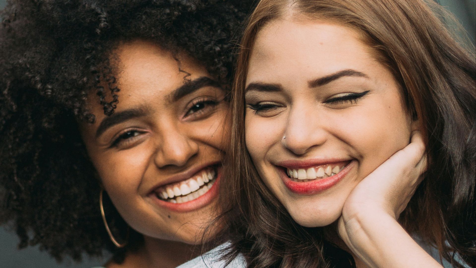 two smiling woman standing near white wall