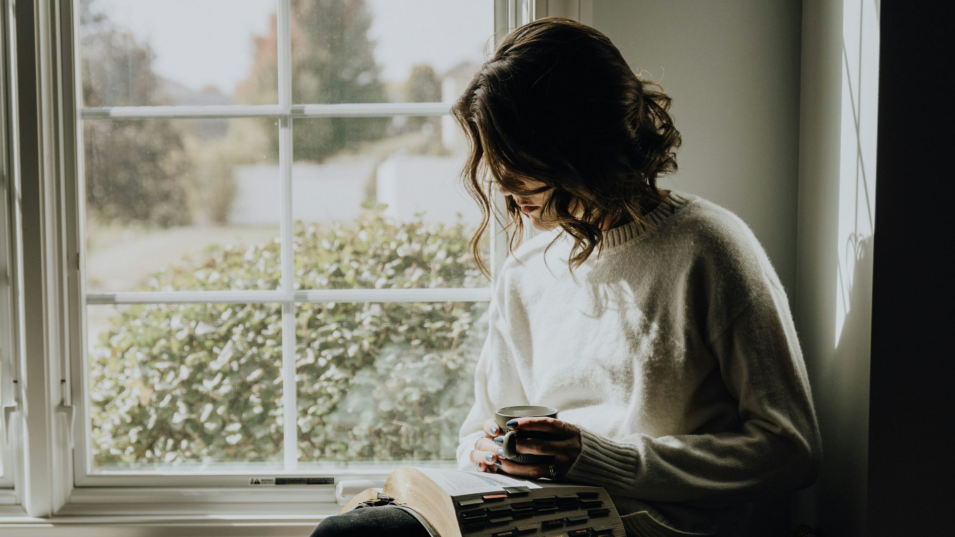 A woman sitting on a window sill reading a book