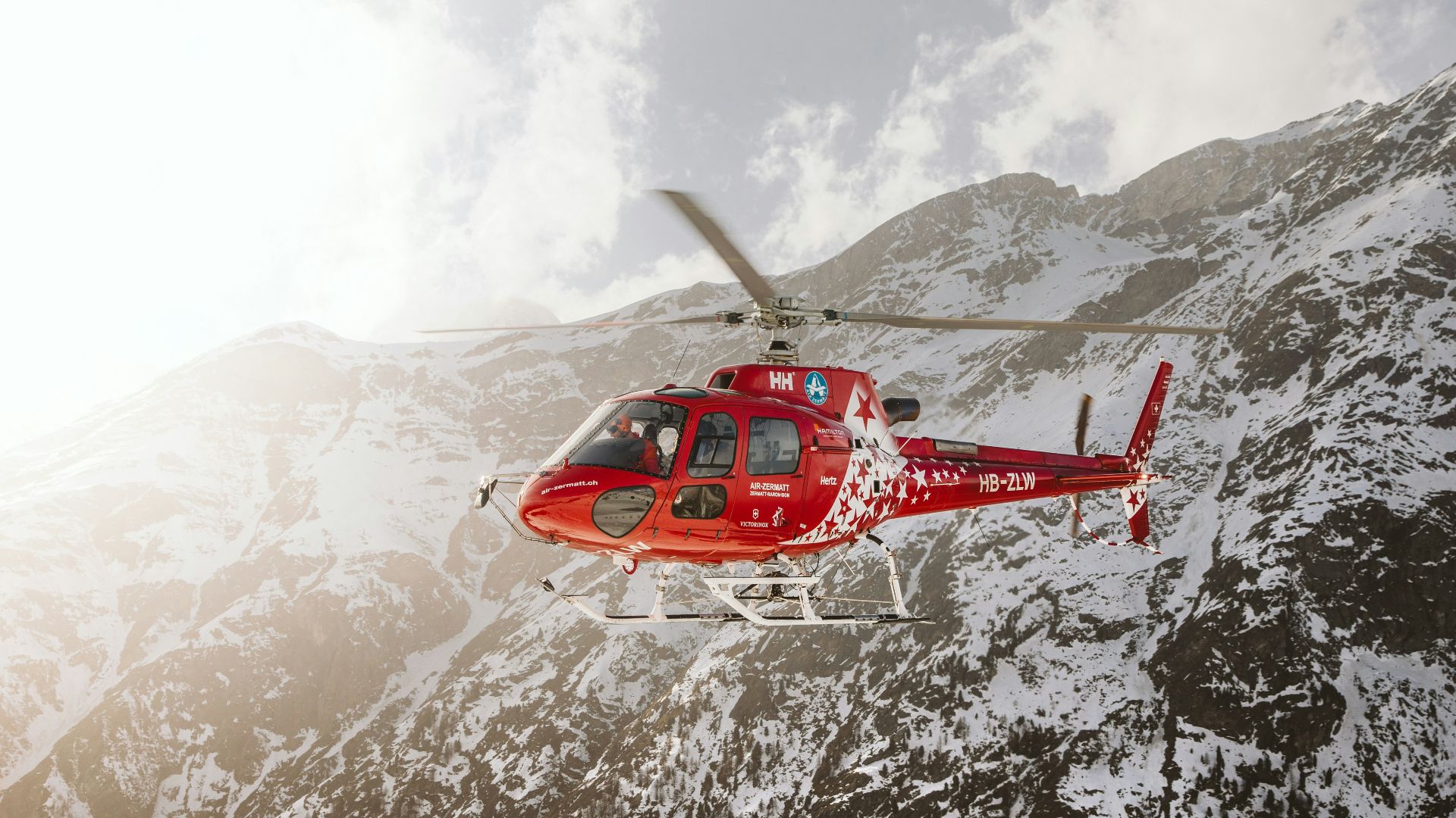 red and white helicopter flying over snow covered mountain during daytime