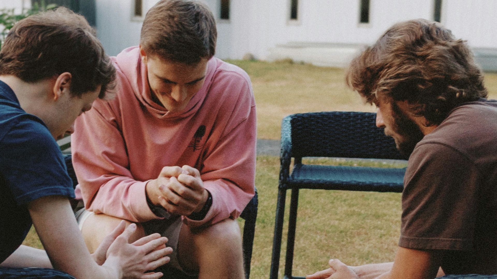 Three young men sitting in a circle praying.