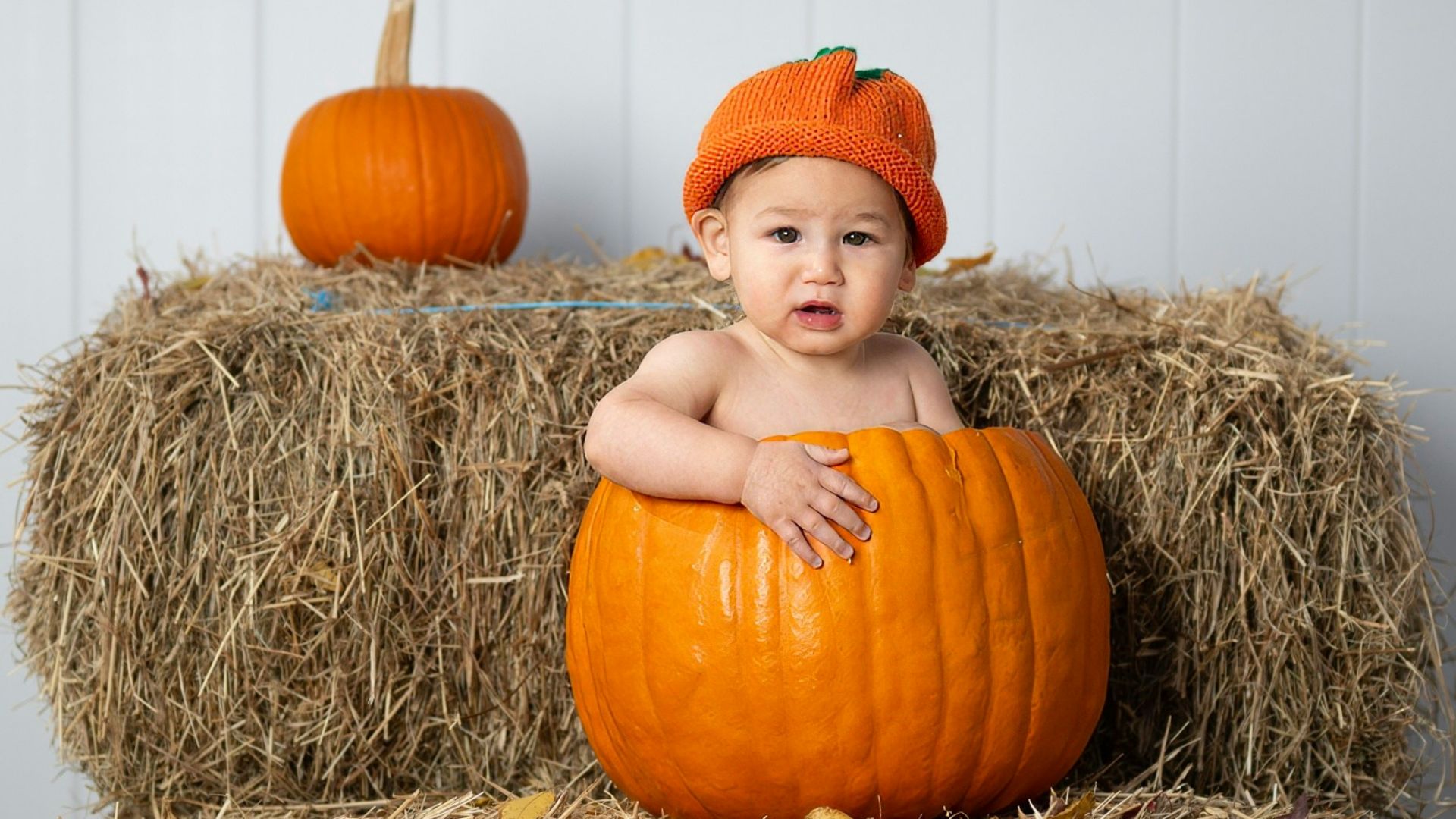 A baby sitting on a hay bale with a pumpkin
