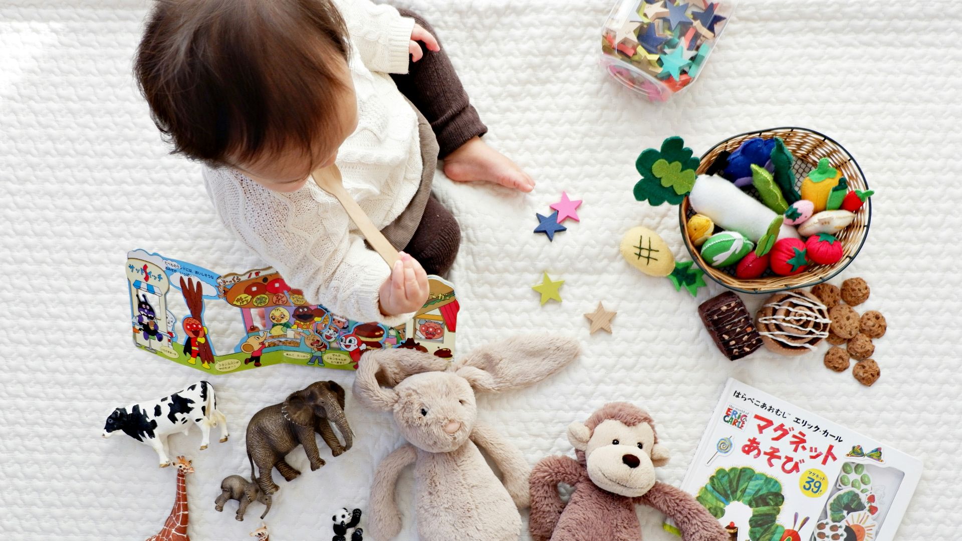 boy sitting on white cloth surrounded by toys