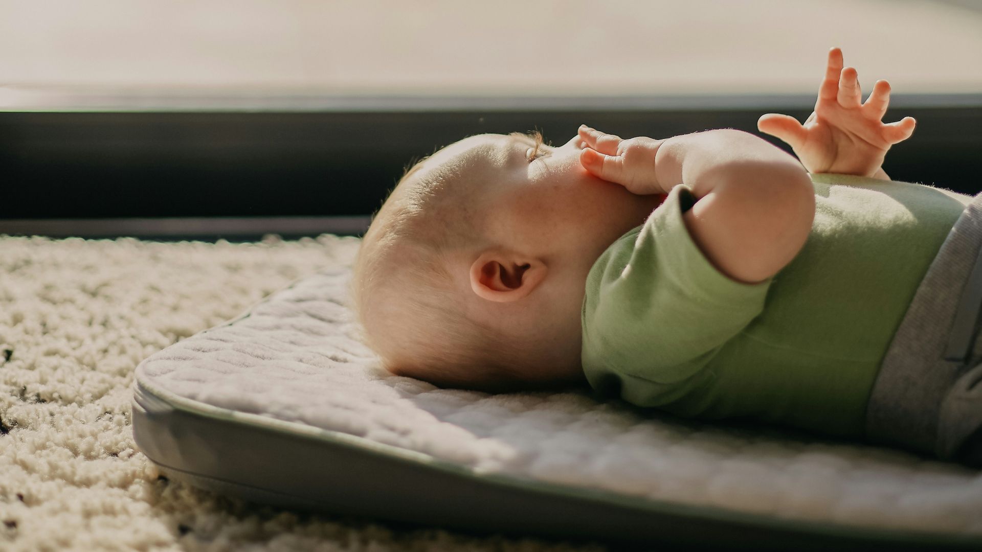 baby in green tank top lying on grey concrete floor