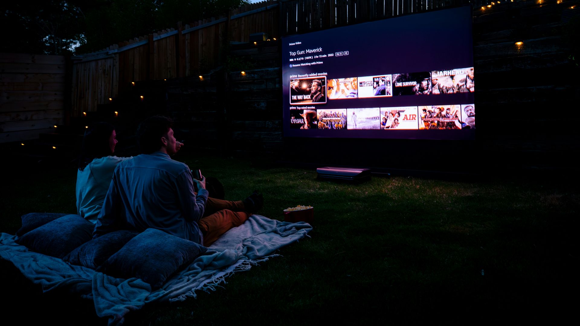 Two people sitting on a blanket watching a movie