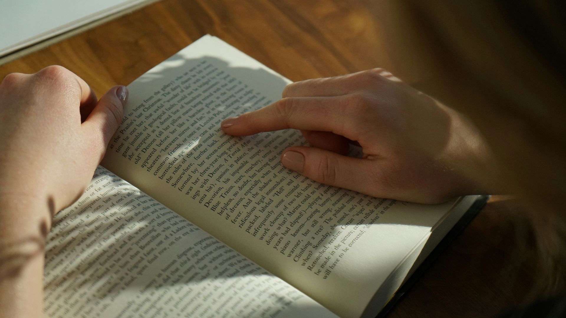 person reading book on brown wooden table taken at daytome